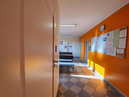 korytarz na parterze, pomarańczowe ściany, tablica ogłoszeń,, popielate ławki dla pacjentów