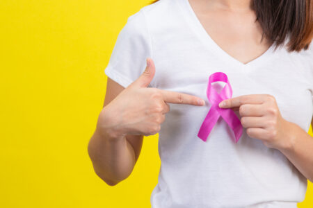 kobieta trzyma przy piersi różową wstążeczkę - symbol walki z nowotworem piersi
