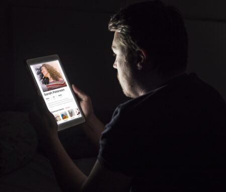 mężczyzna siedzący w ciemnym pokoju i przeglądający tablet