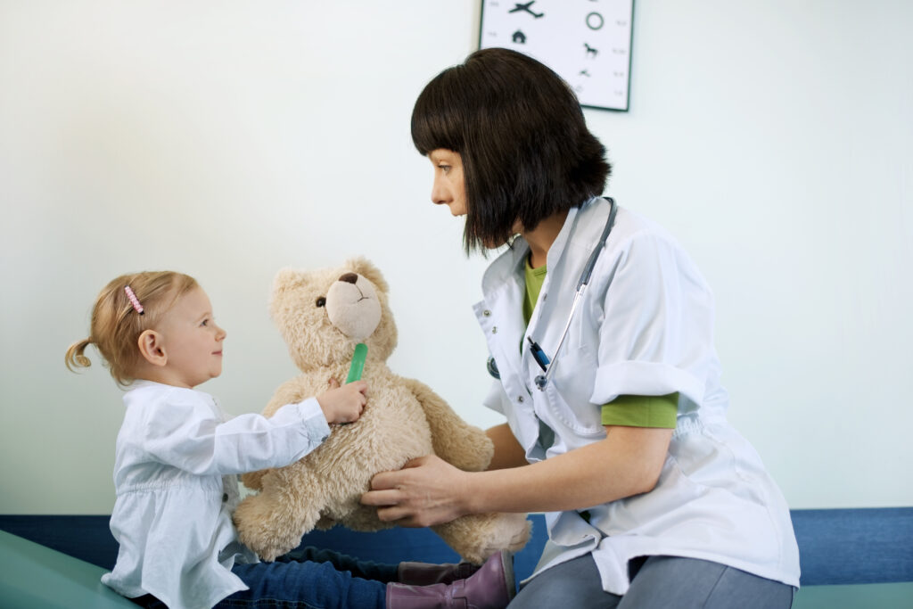 wizyta małej dziewczynki u lekarza pediatry. Osoby na obrazku siedzą i trzymają maskotkę w rękach