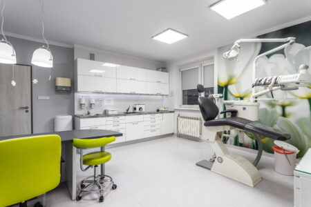 Zdjęcie przestawia gabinet stomatologiczny. Po prawej stronie znajduje się unit, na wprost białe meble (zabudowane góra dół).