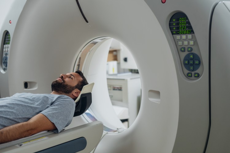 Zdjęcie przedstawia mężczyznę w trakcie wykonywania badania tomografem komputerowym